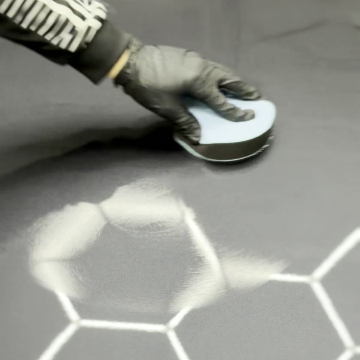 Close-up of ceramic-coated hood — polishing pad reflected in mirror-finish paint with hexagon LED lights