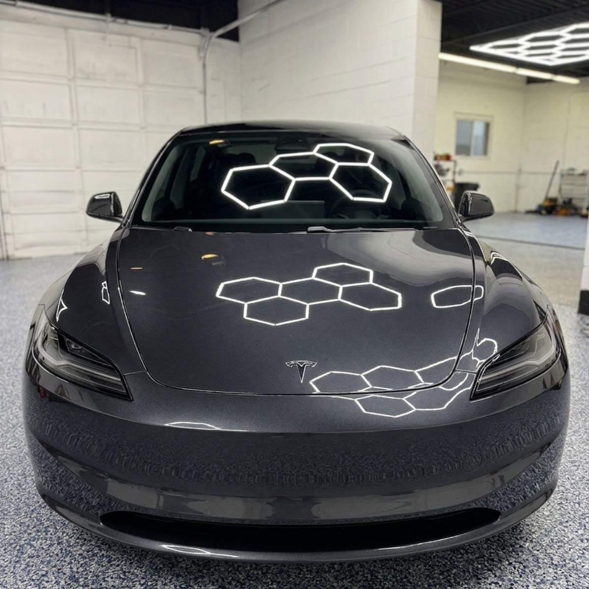 Dark Tesla Model 3 with hexagon light reflections on freshly ceramic-coated hood